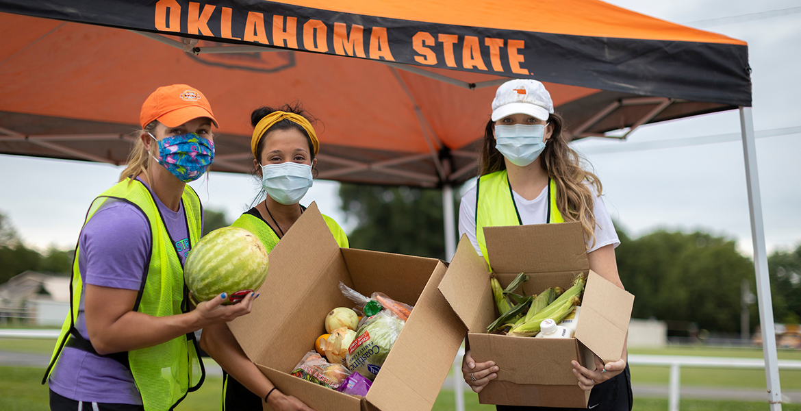 Photo of three masked women handing out food bundles to the needy beneath an OSU tent.