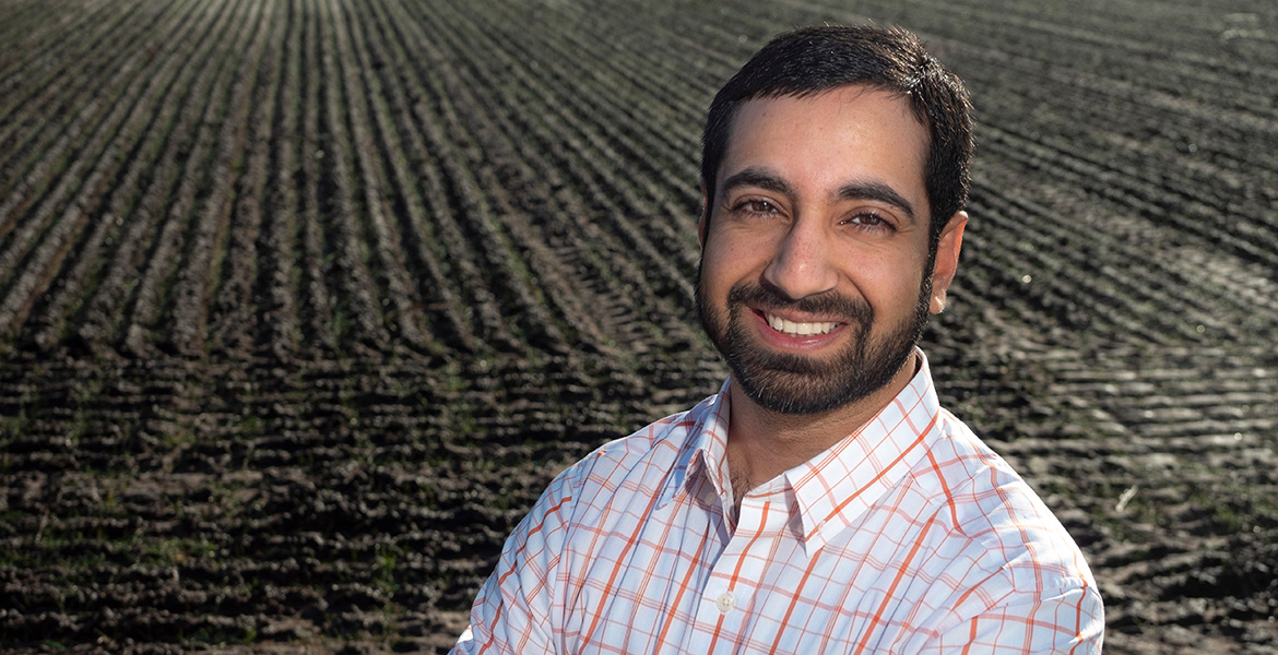 Head and shoulders photo of OSU Irrigation Specialist and Researcher Sumit Sharma with a field prepared fro crops in the background.