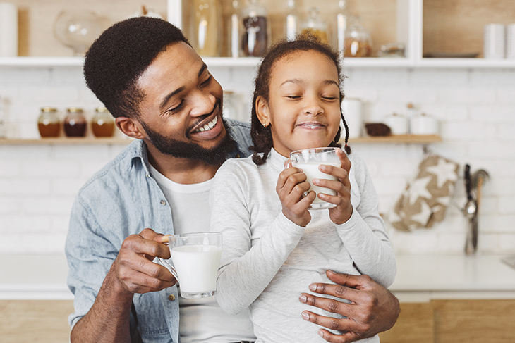 Photo of black man and child drinking milk in a family moment.