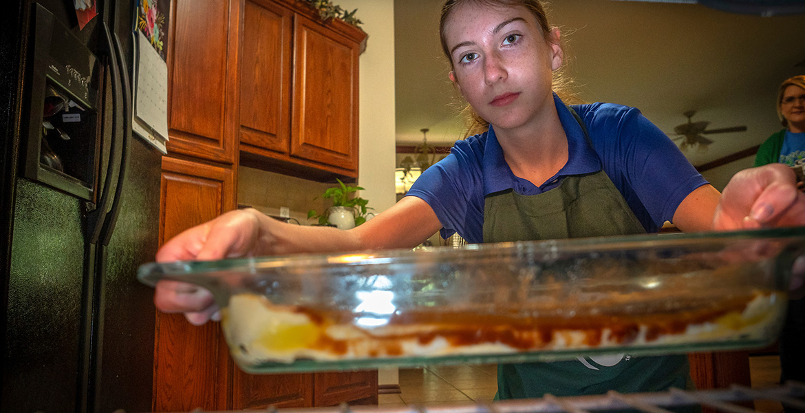 Photo from an inside-the-oven viewpoint of a teenage girl putting a baking dish into it.