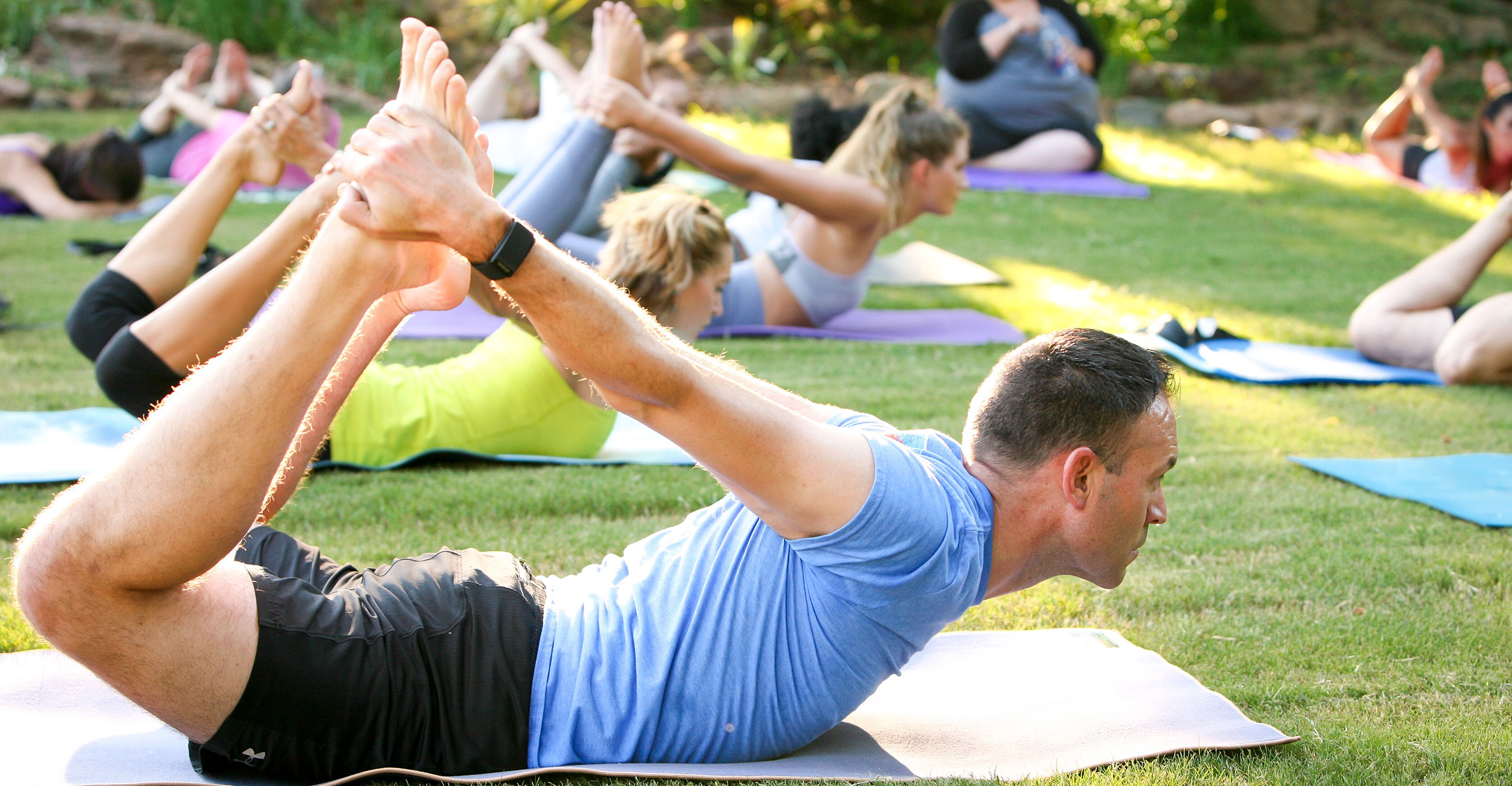 Participants practice yoga poses on mats spread across a grassy lawn during an outdoor group fitness session.