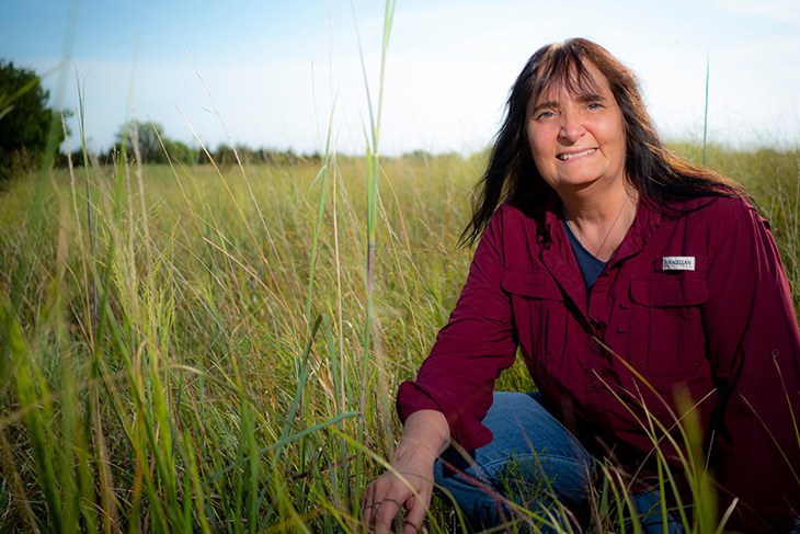 Photo of Gail Wilson kneeling down in grasslands.