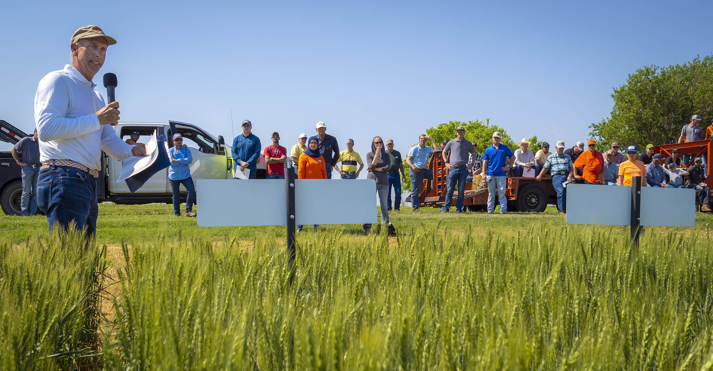 Brett Carver standing in a wheat field with a microphone, speaking at the Lahoma Field Day.