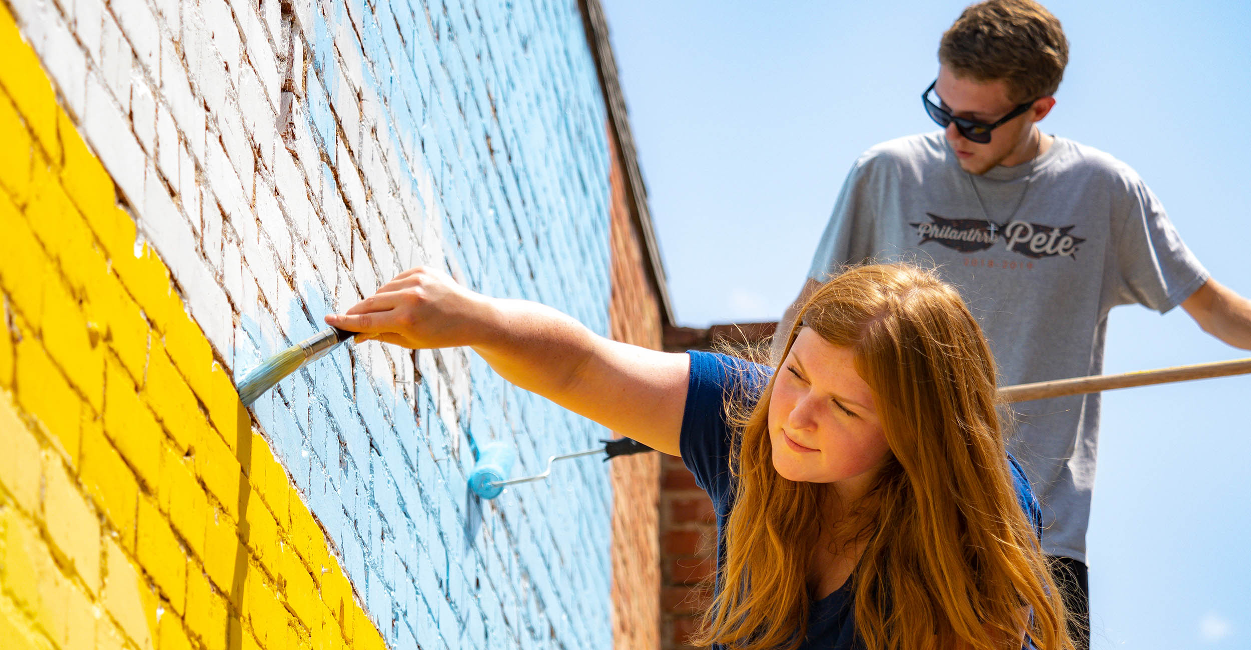 Savy Weston and Hoyt Negben paint a mural on a brick wall.