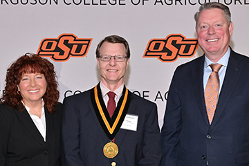 Dan Shoup stands in the middle of the picture, wearing a dark suit and glasses. Cynda Clary, associate dean of academic programs, stands to the left. Jayson Lusk, vice president and dean of OSU Agriculture, stands to the right. All three face the