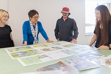Madylan Hux (left) wears a black shirt and smiles at the images on the table. Professor Qing Luo (center left) wears a blue shirt and talks to the group inside a classroom on OSU’s campus. Carson Holmes (center right) and Izzy Holding (right)