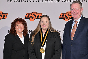 Morgan Pfeiffer stands in the middle of the photo, wearing a medal. Cynda Clary, associate dean of academic programs, stands to the left of the image. Jayson Lusk, vice president and dean of OSU Agriculture, stands to the right. All three face the