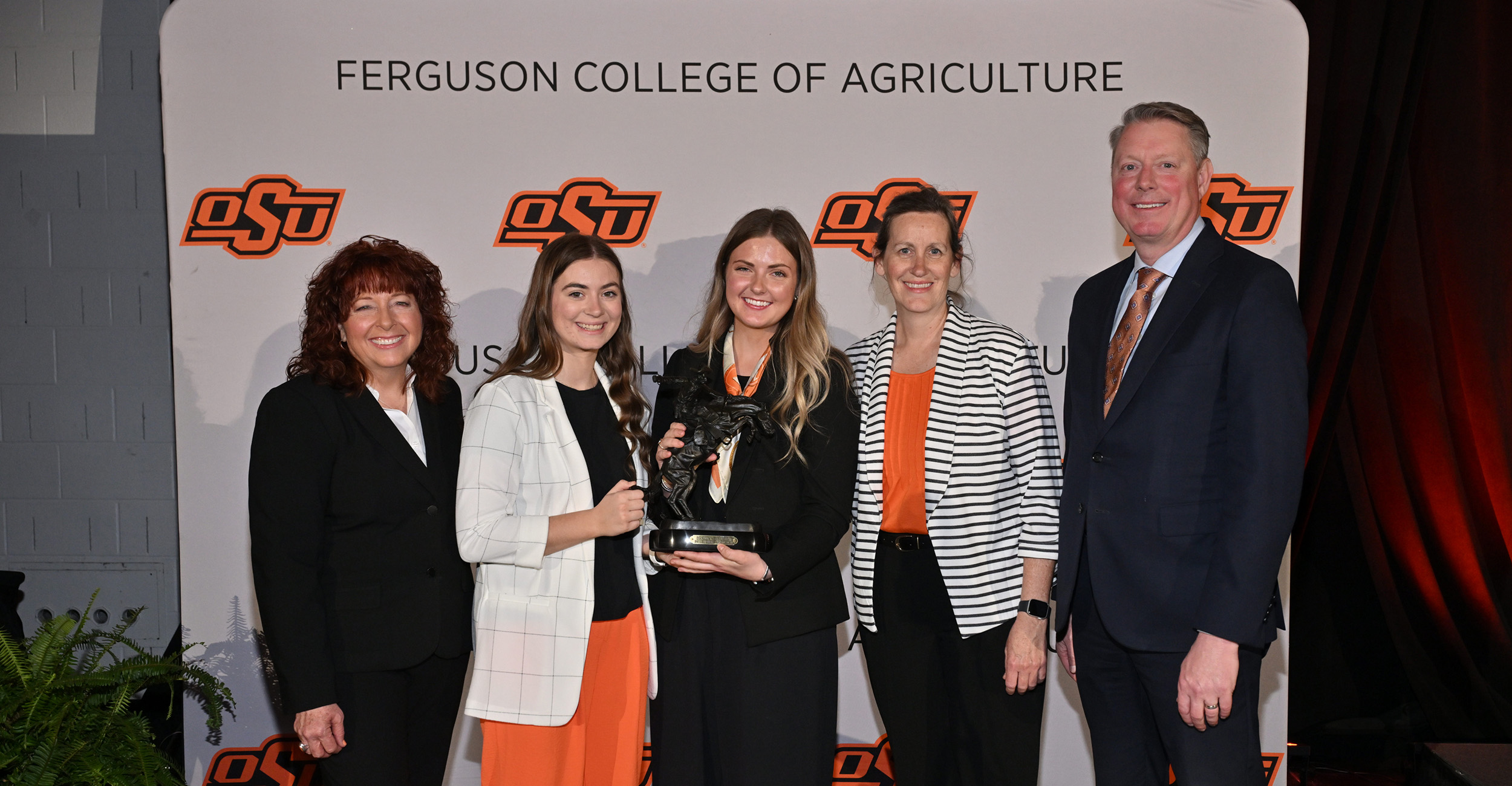 Five people stand together on a stage holding an award in front of a Ferguson College of Agriculture backdrop, indicating a formal university recognition or senior award presentation.