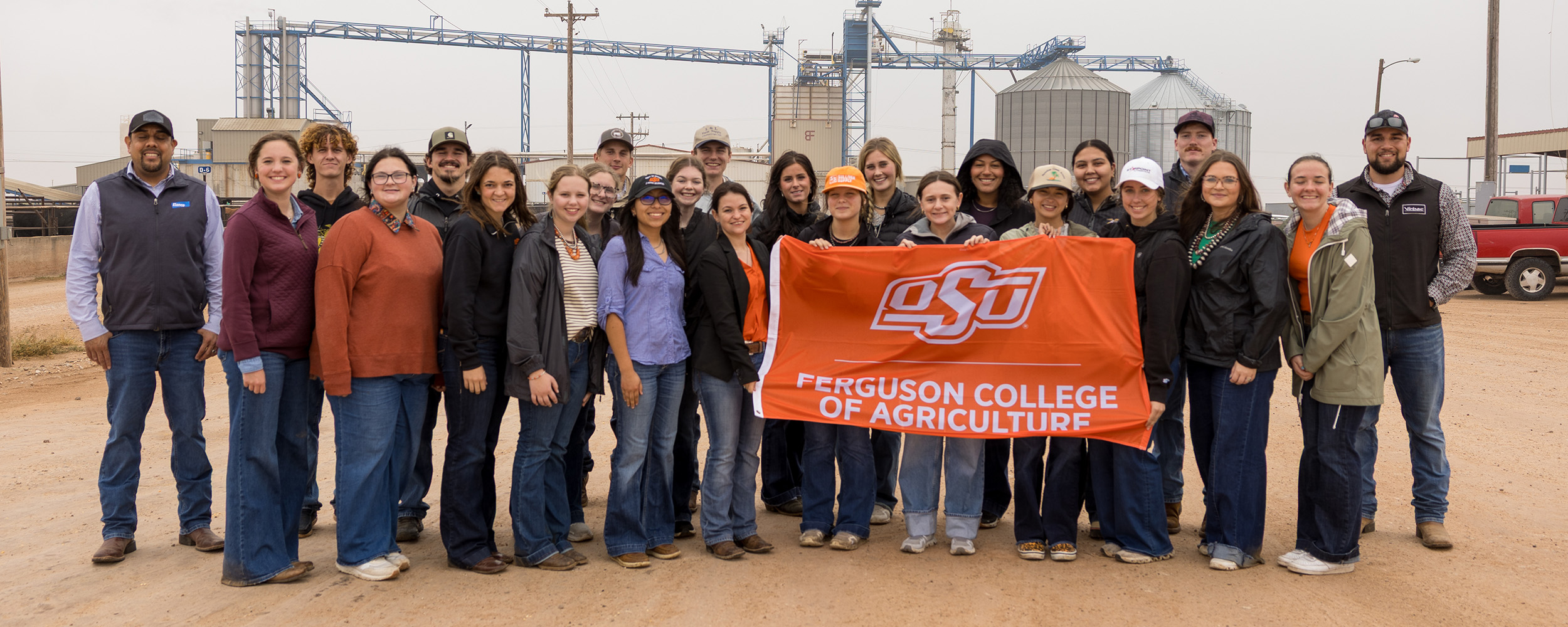 A large group of Ferguson College of Agriculture students gather for a photo in an agricultural setting. They are holding a Ferguson College of Agriculture flag.