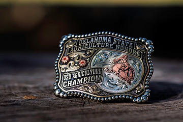 OSU Agriculture Champion custom-made buckle displayed on a wooden surface.