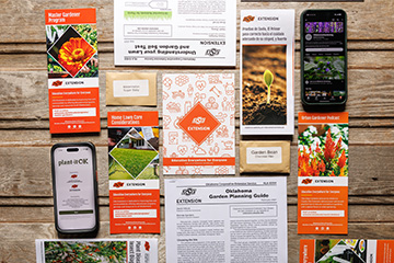 Flat lay of Oklahoma State University Extension gardening resources, including brochures, seed packets, printed guides, and smartphone screens, arranged on a wooden surface to highlight available gardening education tools.