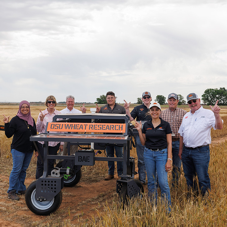 OSU faculty and staff and students stand next to the wheat cart in a wheat field.