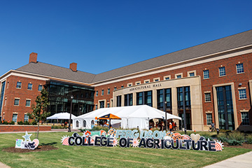 A Ferguson College of Agriculture sign outside of Agricultural Hall with tailgate tents in the background.