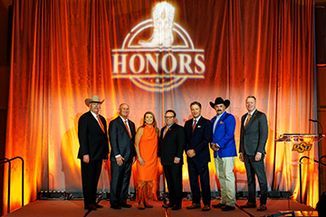 Randy Ratliff, Joe Caughlin, Claudia Humphreys, Marc Conrady, Mark Vaughan, Mark Shaw and Jayson Lusk standing on a stage in front of an orange curtain with the Honors emblem.