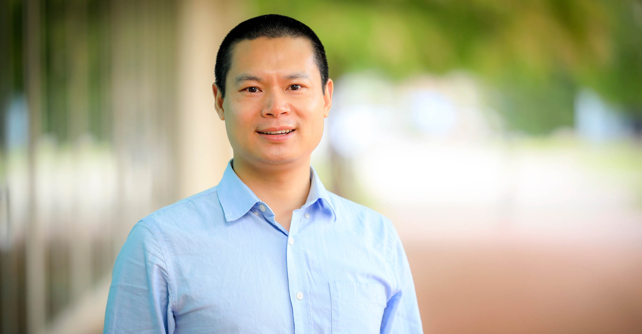 Headshot of Professor Yong Cheng in a light blue button-up dress shirt. The background is blurred.
