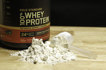 Jar of protein powder with protein powder in the foreground with a plastic scoop.