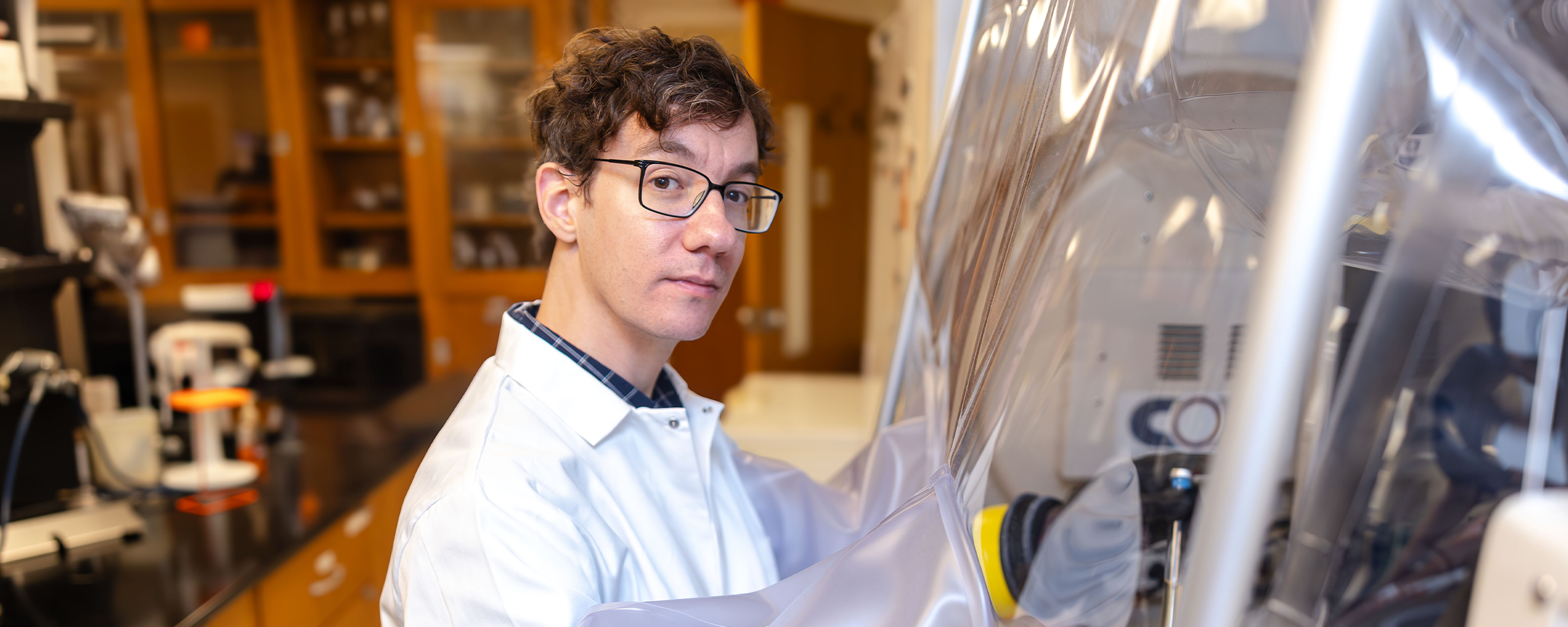 Dr. Paul Kirchberger wears a white lab coat and works with equipment inside a sealed laboratory glove box.