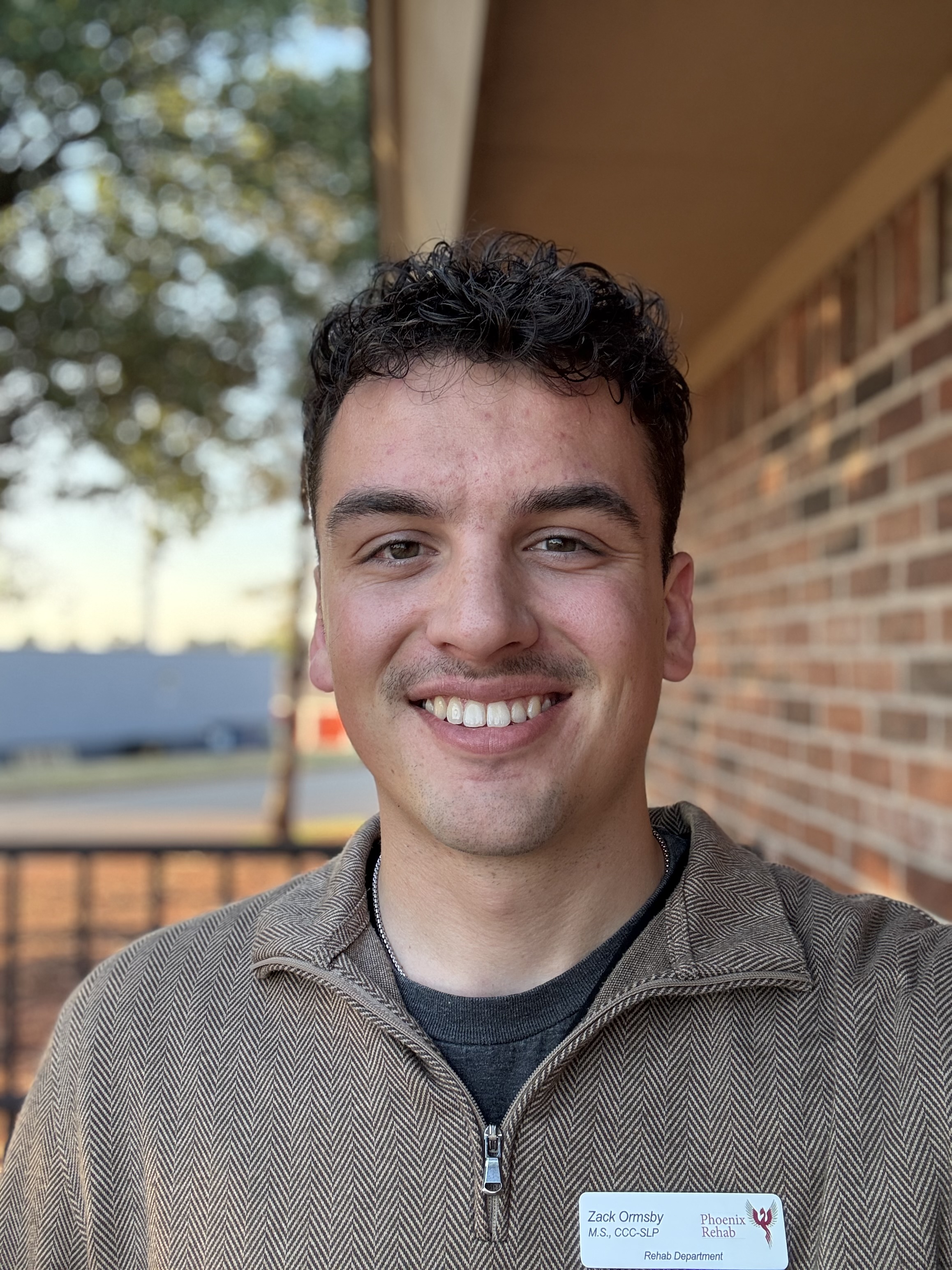 Zachary Ormsby, an Oklahoma State University alumnus and speech-language pathologist, smiles for a portrait outdoors.