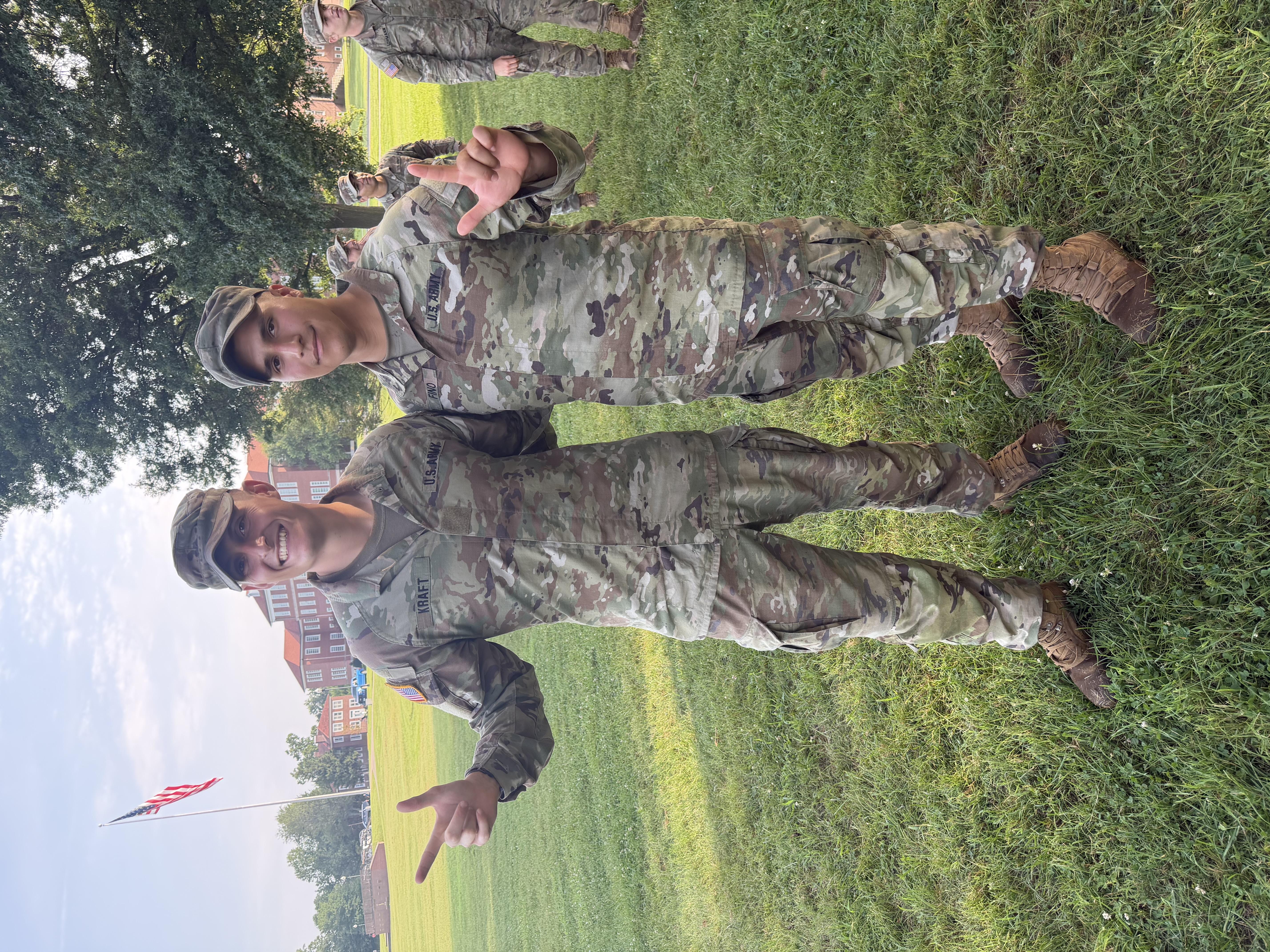 Hector Fino and another Army ROTC cadet pose together in uniform on a grassy field.