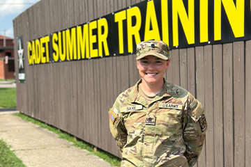 Emma Saxe stands in uniform in front of a Cadet Summer Training sign.