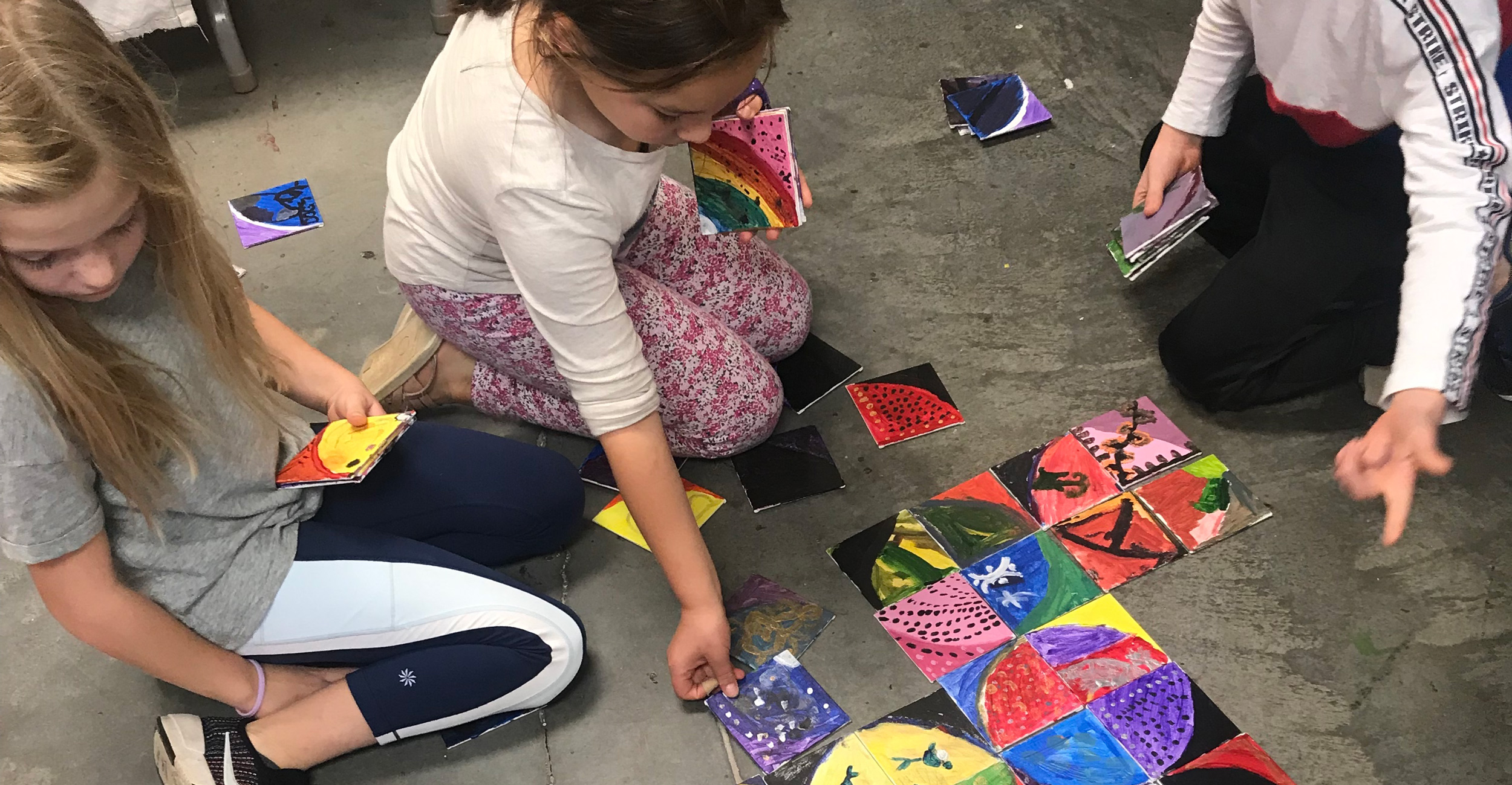 Kids arrange paper artworks on the floor of the Prairie Arts Center.