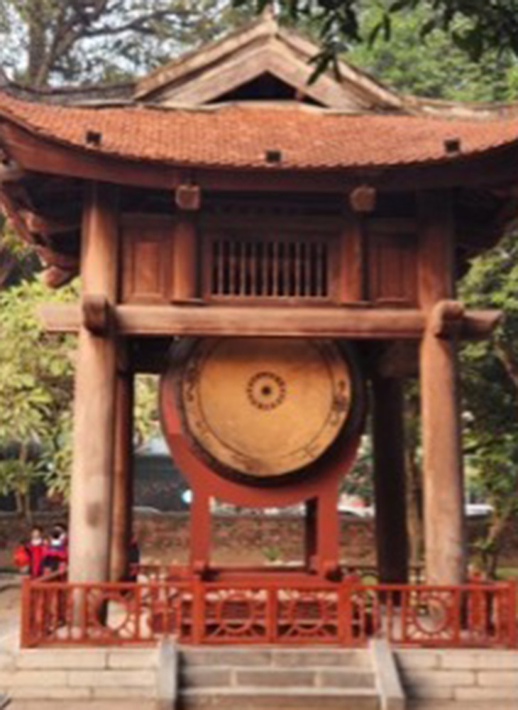 A traditional wooden pavilion houses a large ceremonial drum, set within a courtyard surrounded by trees and historic architecture.
