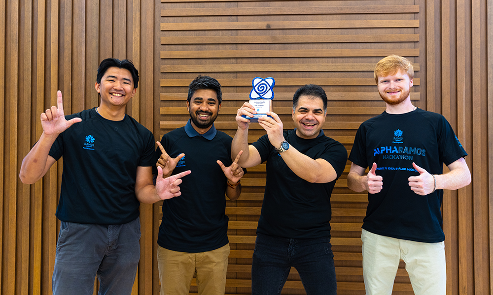 Four students celebrate winning. One holds up a trophy. They all smile.