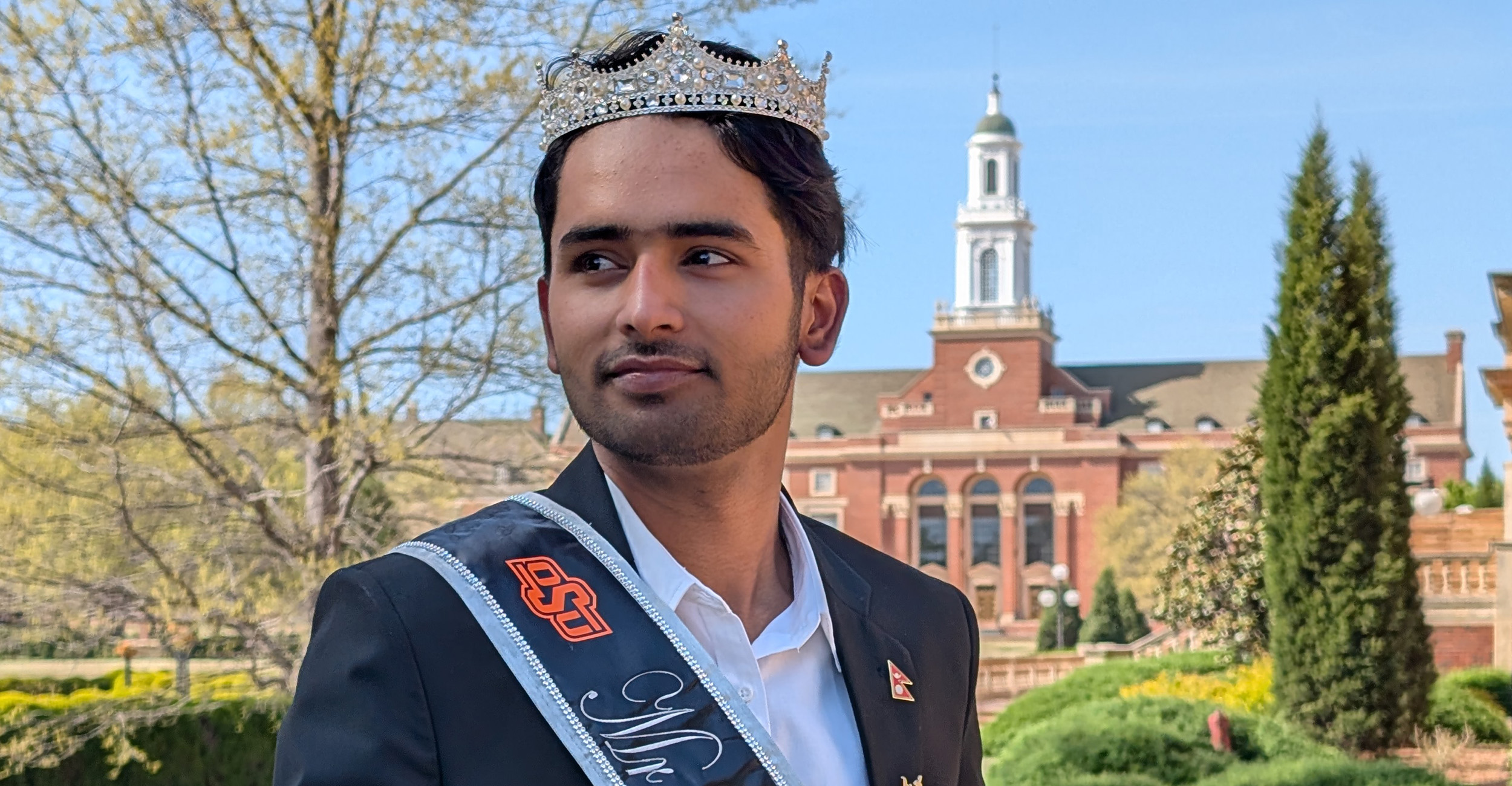Ayush Bhattarai wears his Mr. International crown and sash. He stands outside Edmon Low Library.