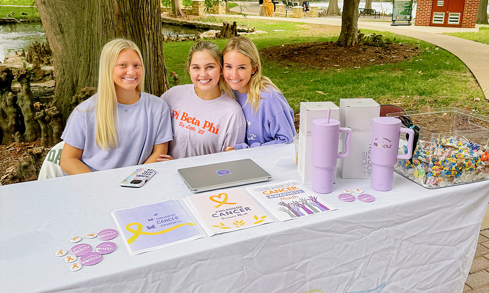 Pi Phi sorority members sit at a table promoting philanthropy