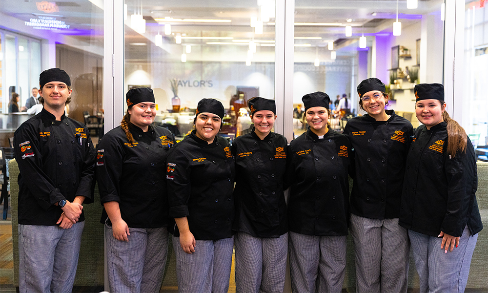 Smiling chef students lined up in their new black and orange chef uniforms.