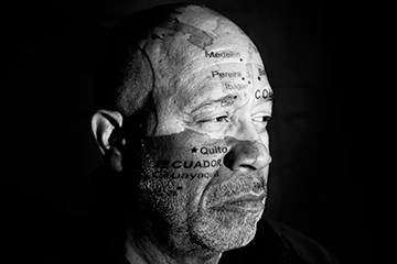 A closeup of Dr. Craig Watters' face features a map of Ecuador projected onto it. This is a black-and-white photo.