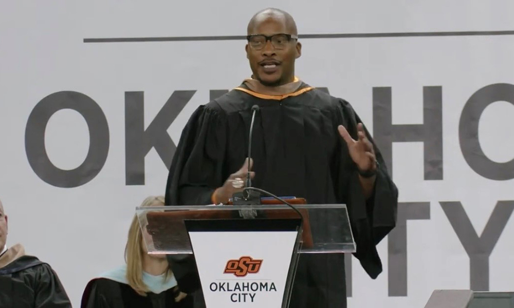 Donovan Woods stands at the lectern and talks into the microphone at OSU-OKC's graduation.