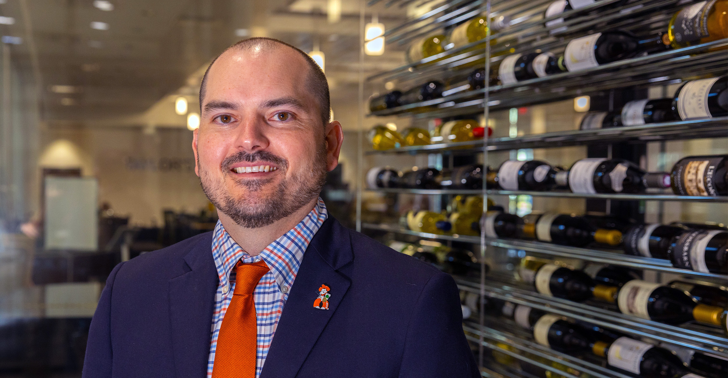 Kyle Bunds poses in a suit while wearing an orange tie inside the wine cellar at Taylor's Restaurant