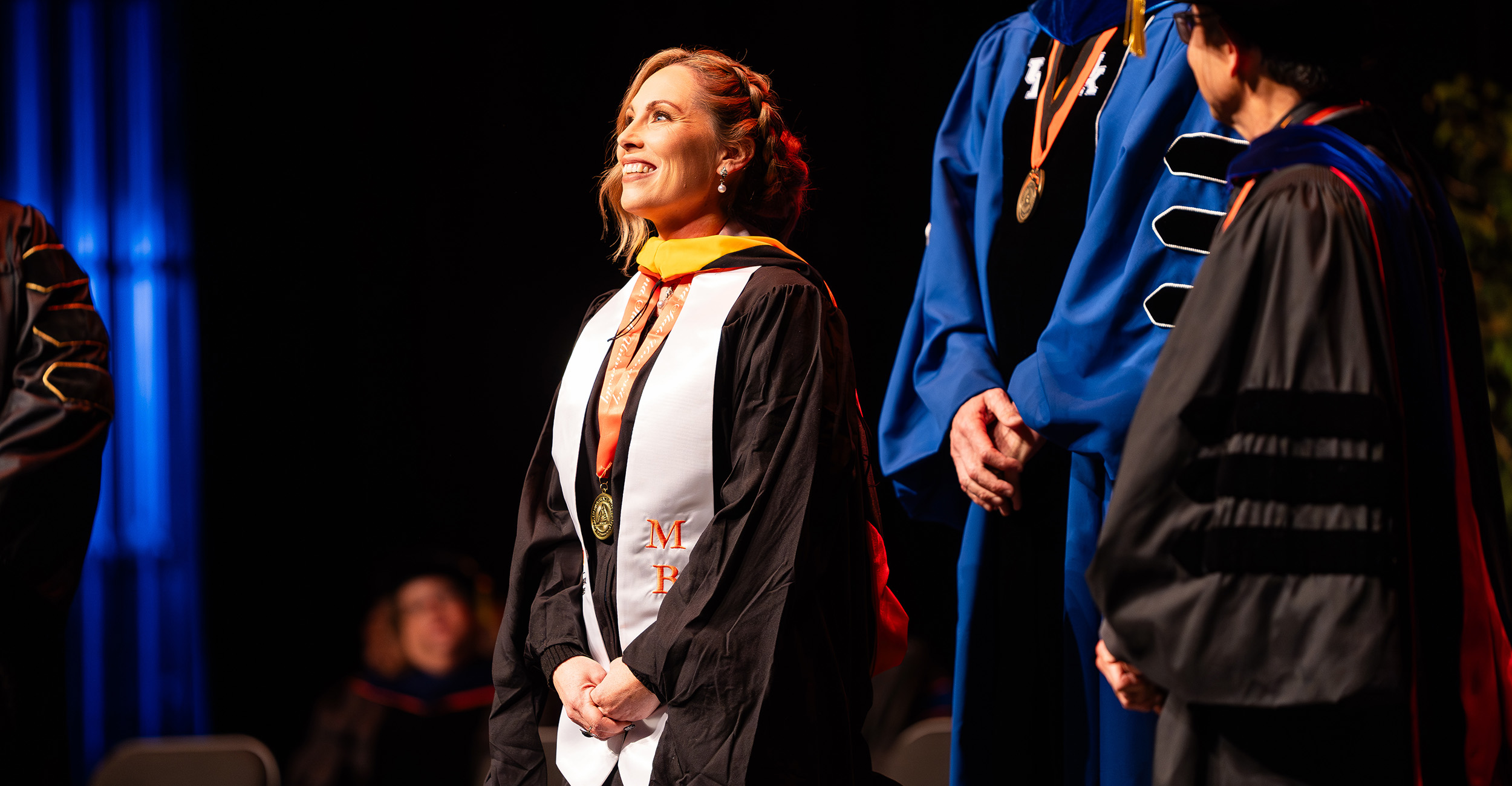 An MBA graduate has her hood placed on during a graduation ceremony.