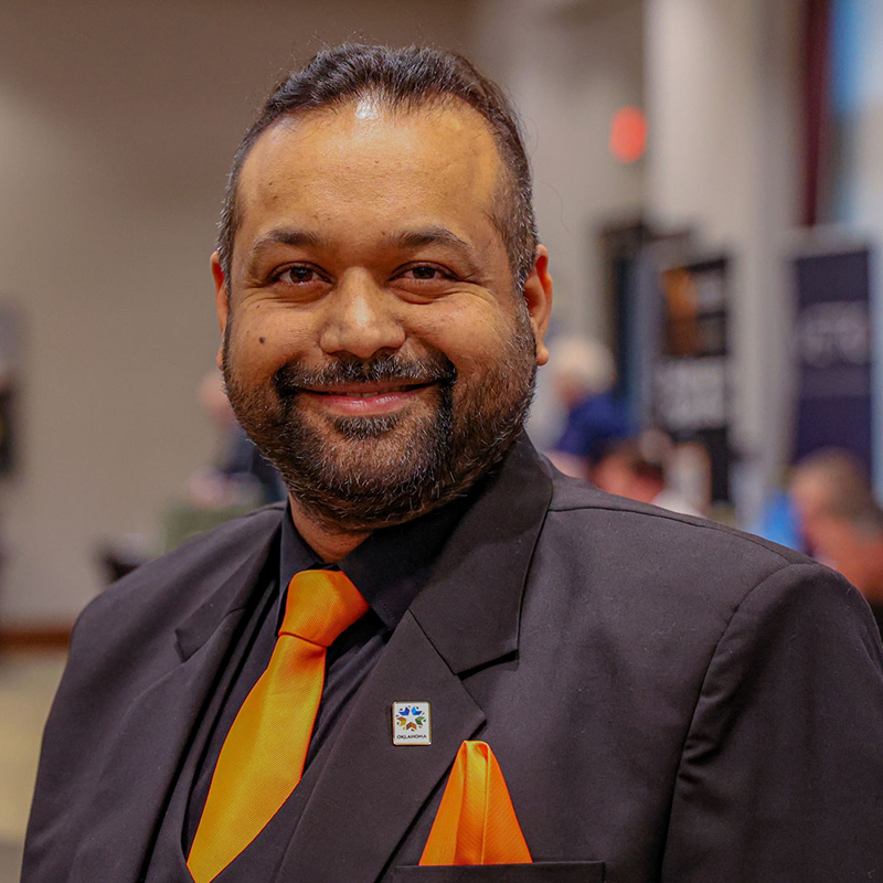 Sachin Gupta, dressed in a suit with an orange tie, smiles for a portrait.