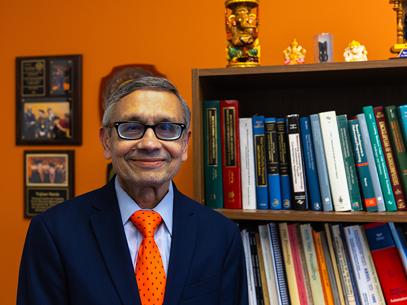 A professor stands in front of his bookshelf.