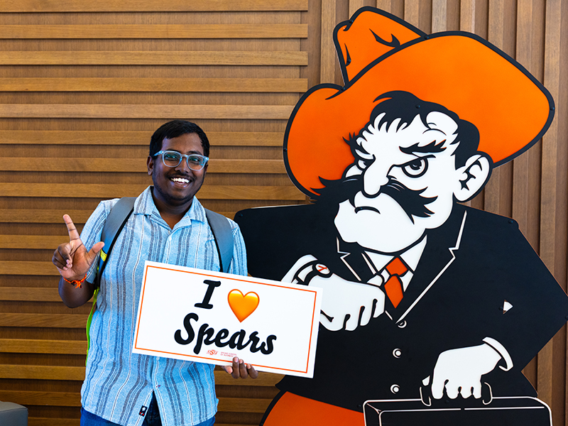 A student poses with Business Pete and holds an I Heart Spears" sign.