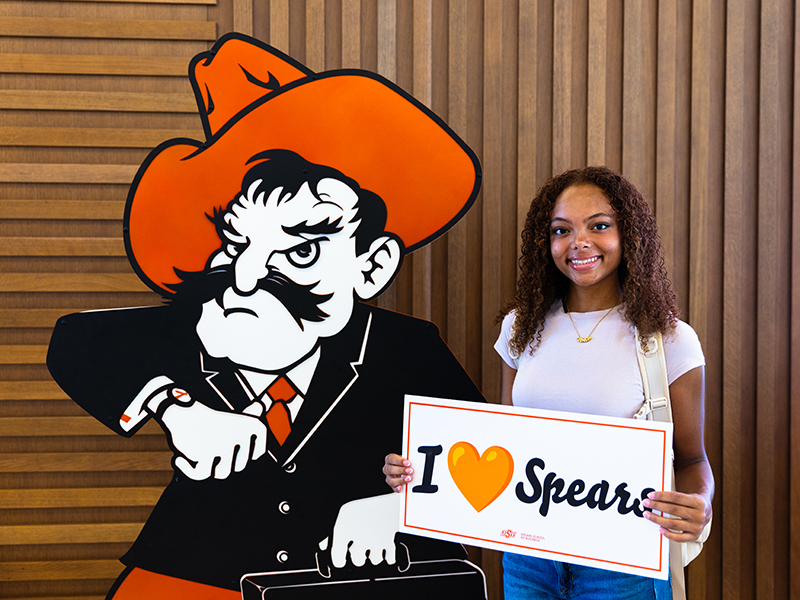 A student poses with Business Pete and holds an I Heart Spears sign.