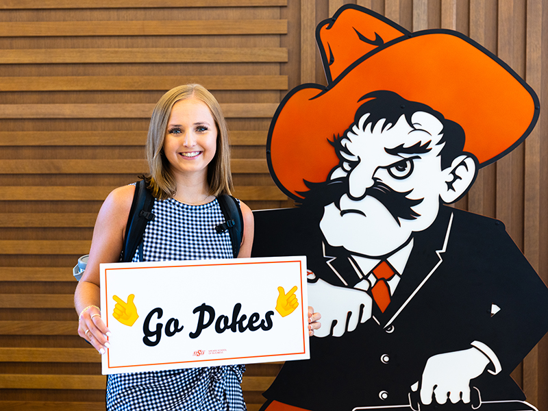 A student poses with Business Pete and holds a Go Pokes sign.