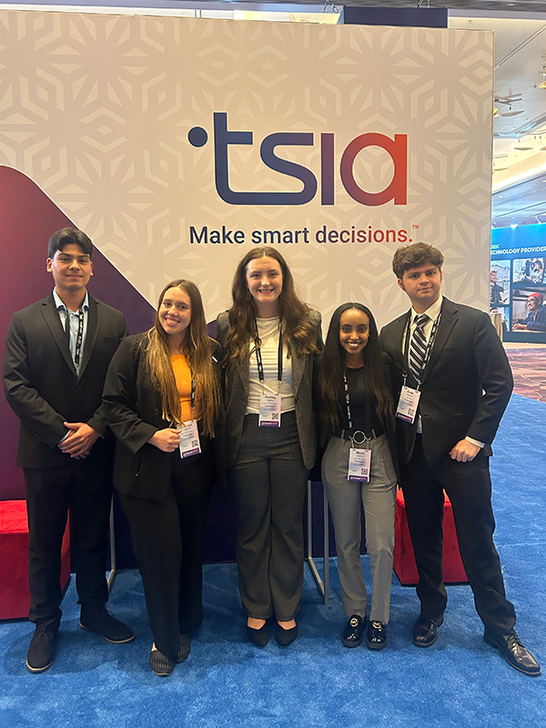 Five students dressed in business attire stand in front of a TSIA sign.