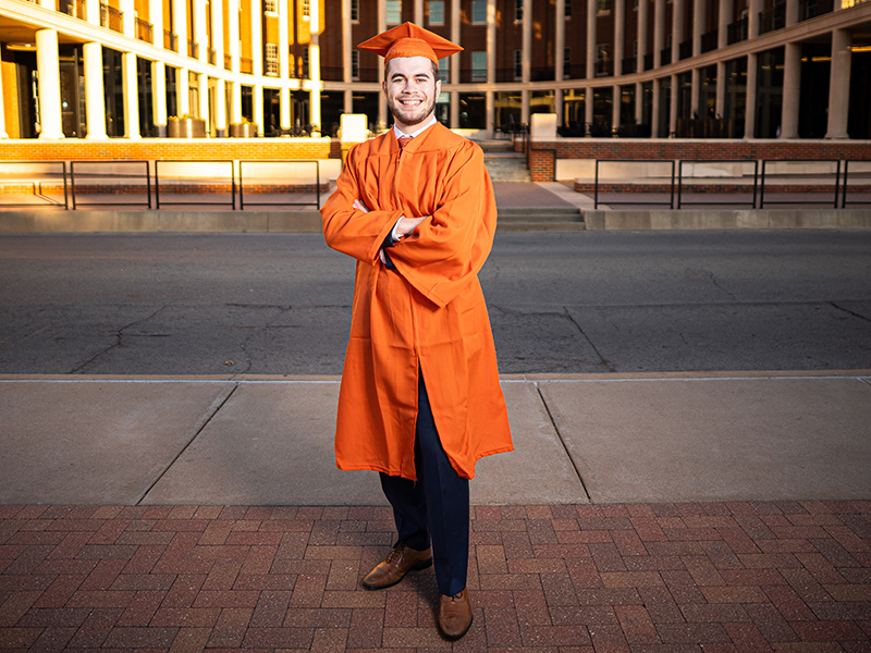 Wesley Cannatti smiles as he wears his orange cap and gown and stands outside the Business Building. Receiving the orange gown is a big honor.