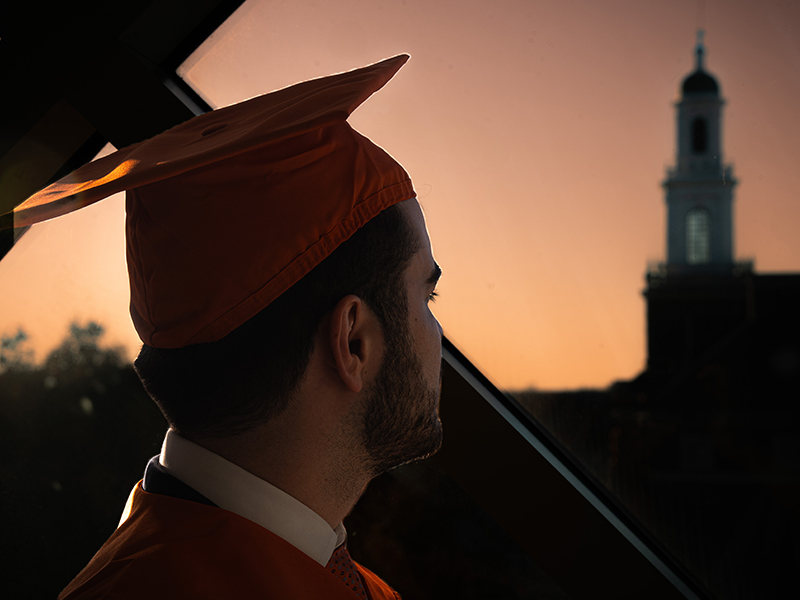 Wesley Cannatti wears his orange cap and looks out a Business Building window. The photo captures his reflective mood as he prepares to graduate.