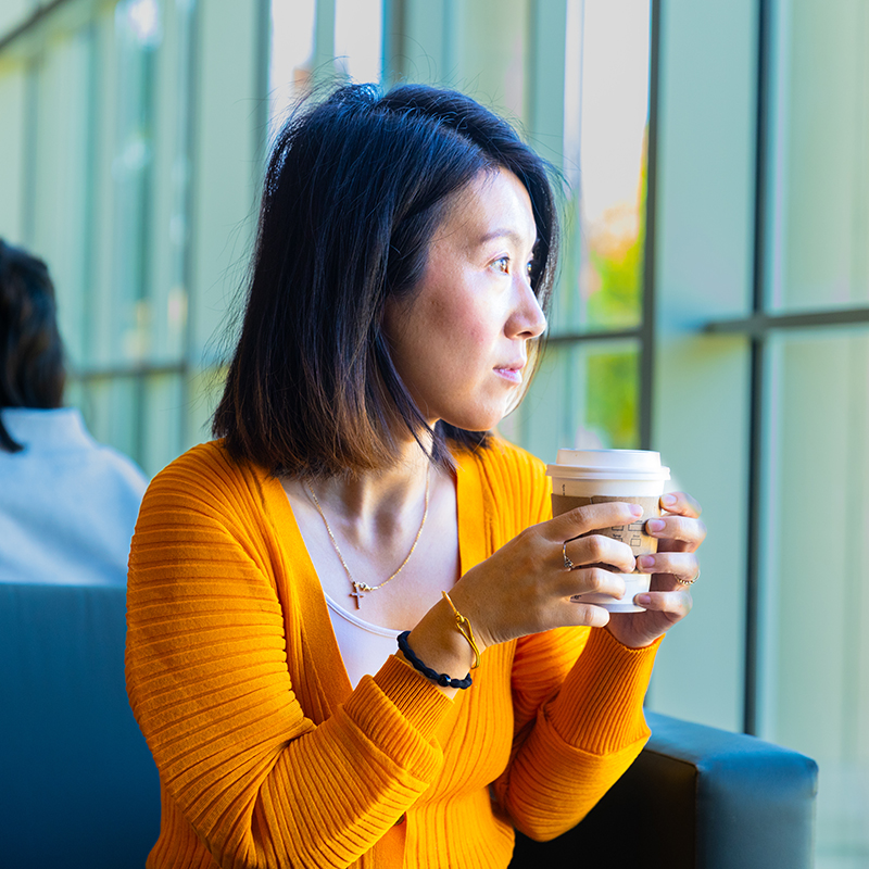 Yuechen Wu holds a coffee cup and looks out the window.