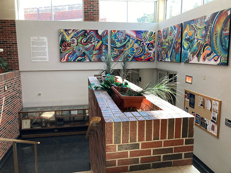 Color photograph of an indoor brick stairwell with a planter ledge and decorative wall-mounted plant shelves, lit by natural light from high windows.