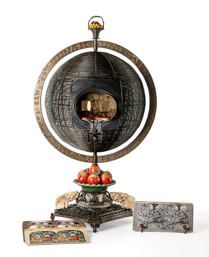 Decorative antique stereoscope viewer with a circular frame and ornate base displayed alongside stereograph cards against a plain background.