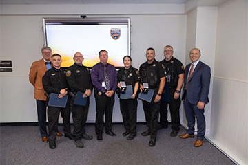 A group of university officials and OSU Police officers pose for a photo during a recognition ceremony, with several officers holding certificates and awards in front of an OSU Police display screen.