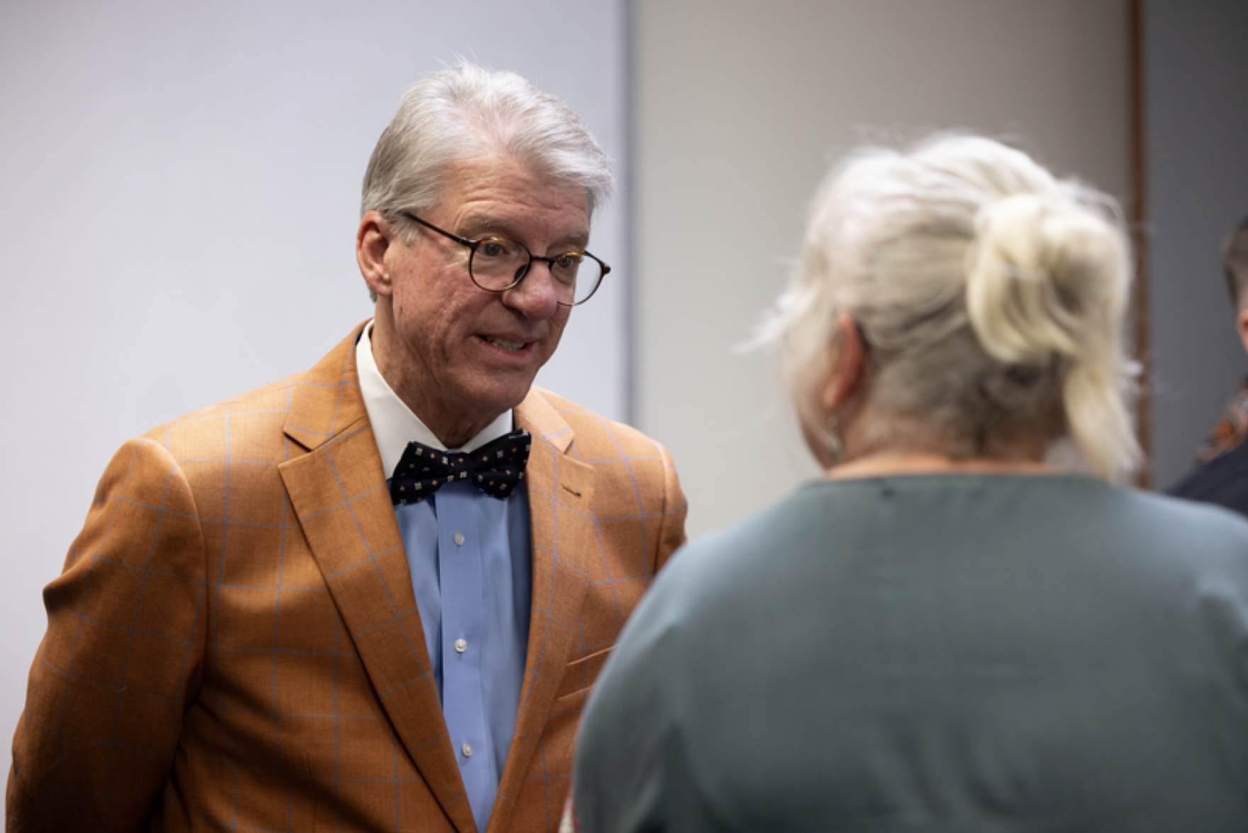 A university official wearing a plaid sport coat and bow tie speaks with an attendee during an OSU Police recognition event.