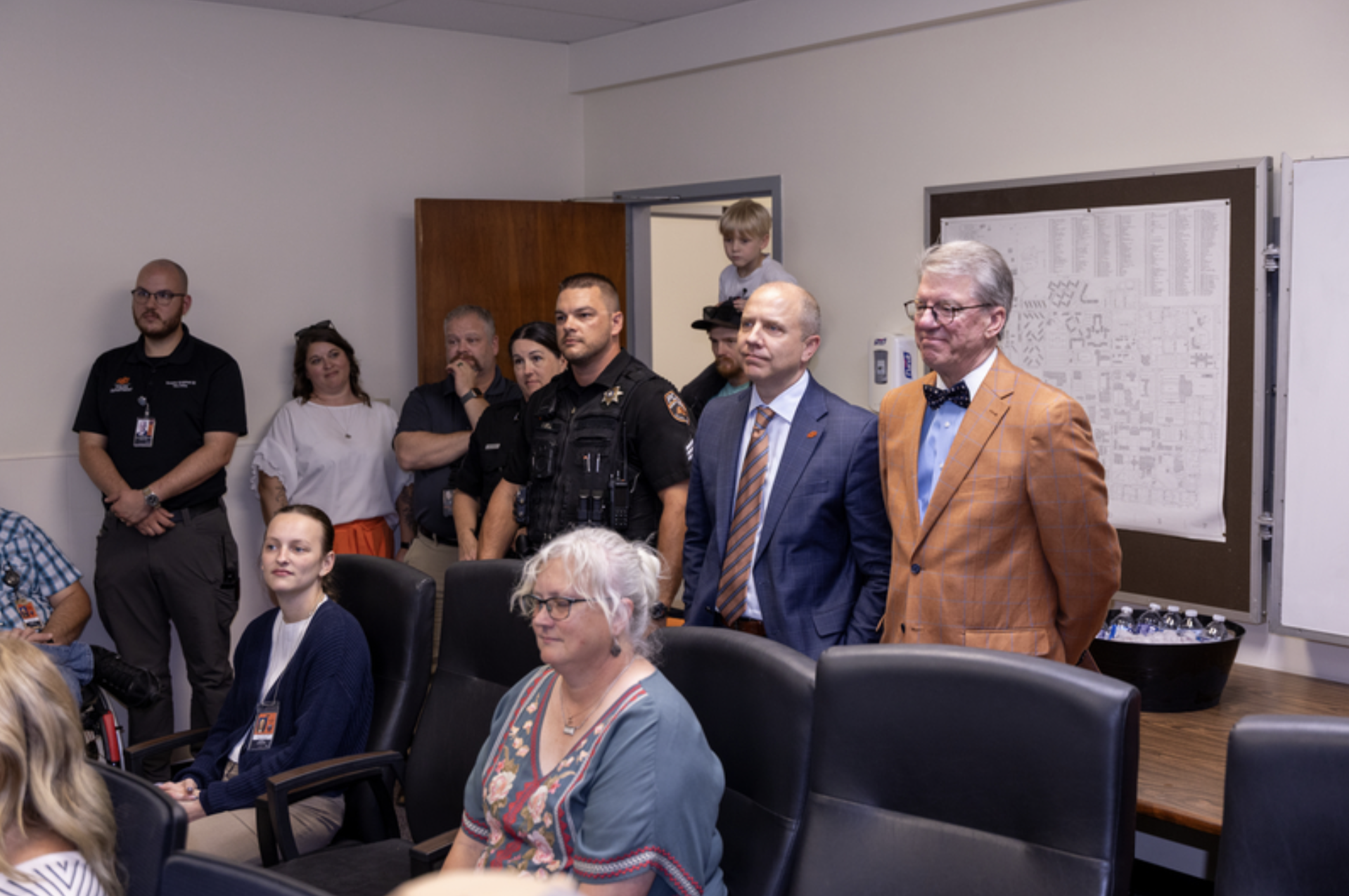Attendees, including a uniformed police officer and university officials, stand and sit in a conference room during an OSU Police recognition or swearing-in ceremony.