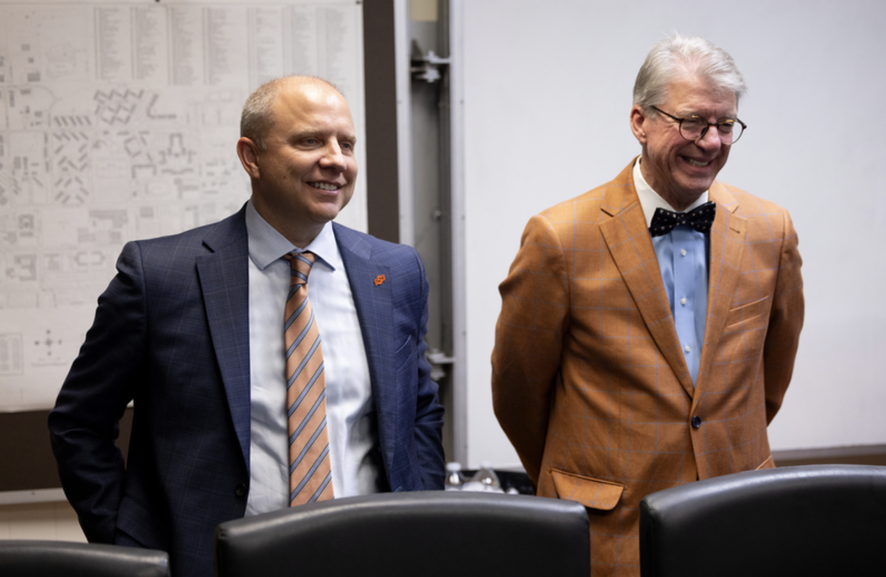 Two university officials stand in a conference room during an OSU Police recognition ceremony, with meeting chairs and a campus map visible in the background.