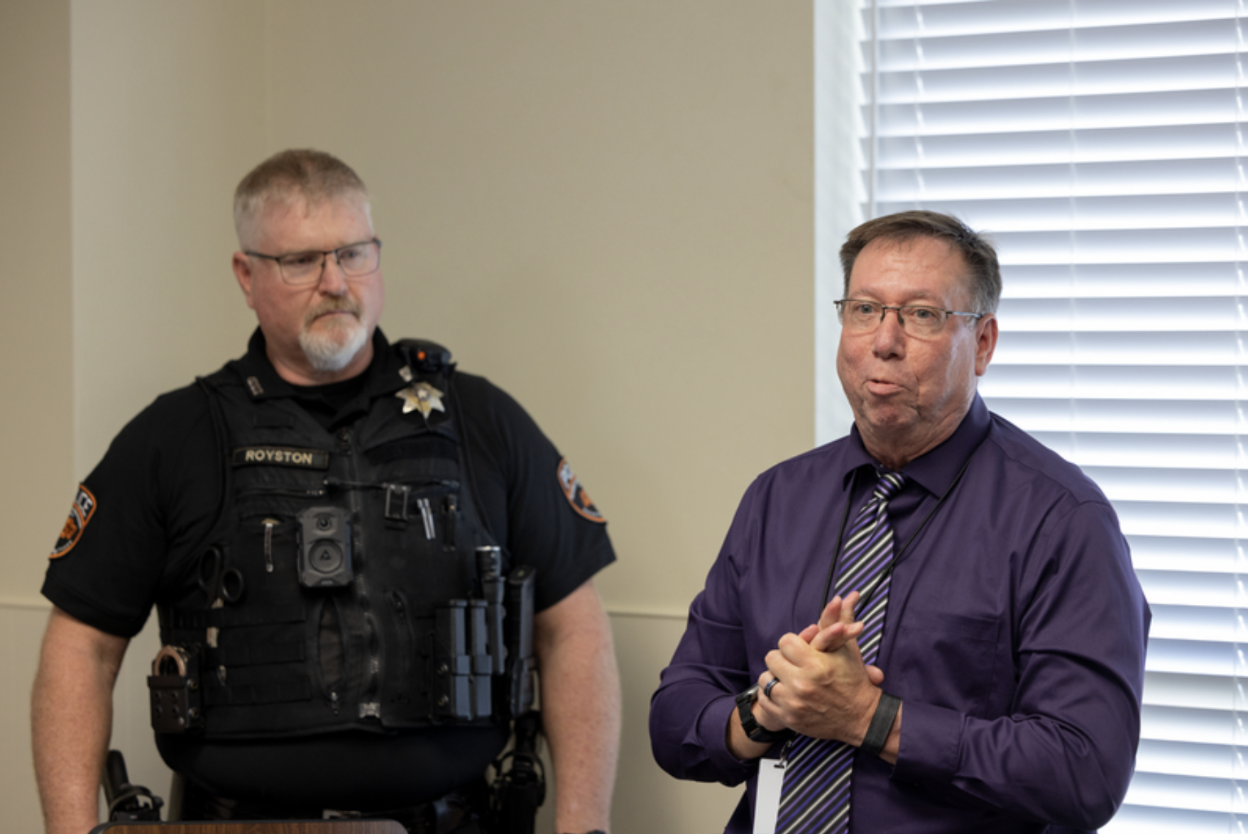 A presenter speaks beside a uniformed OSU Police officer during a recognition ceremony in a meeting room.
